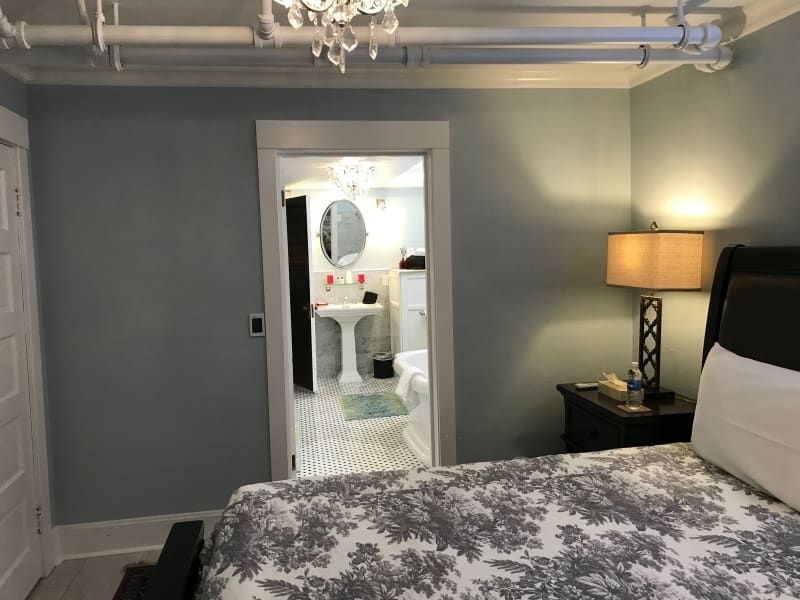 A bedroom with a bed and a lamp looking into a bathroom.