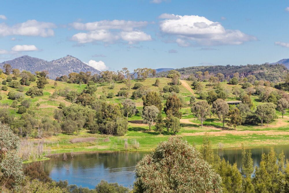 A Lake Surrounded by Trees and Grass With Mountains in the Background — Tamworth Interiors in Scone, NSW