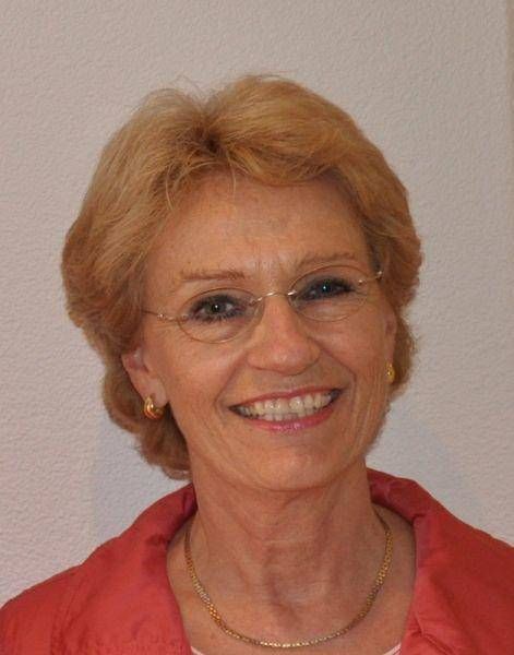 Junge Person mit geflochtenen Haaren lächelt, im Freien, weicher Hintergrund.