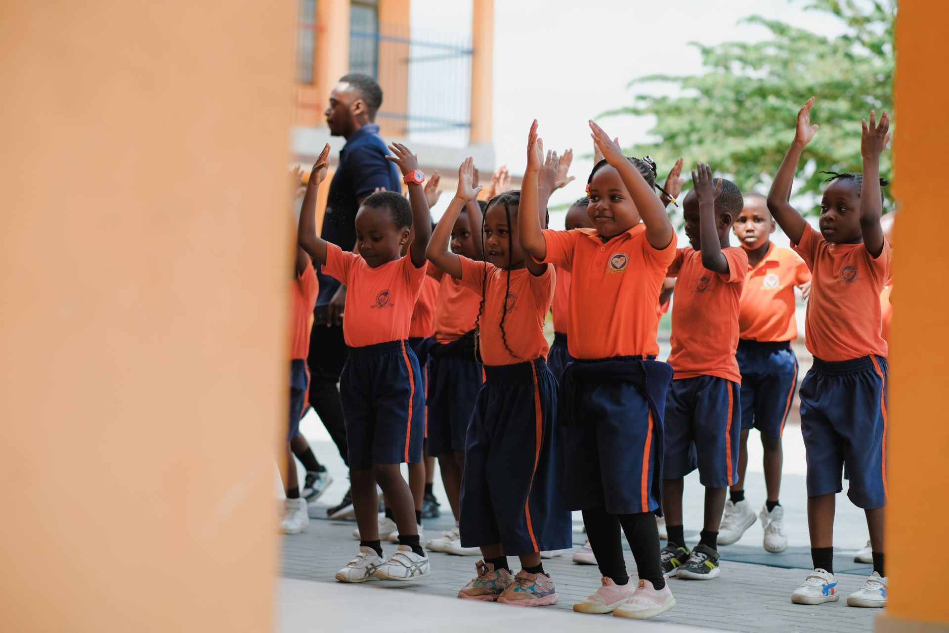 Schulkinder in orangefarbenen Uniformen heben im Freien während einer Gruppenaktivität die Arme.