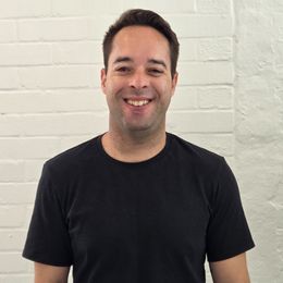 A man in a black sweater is smiling for the camera.