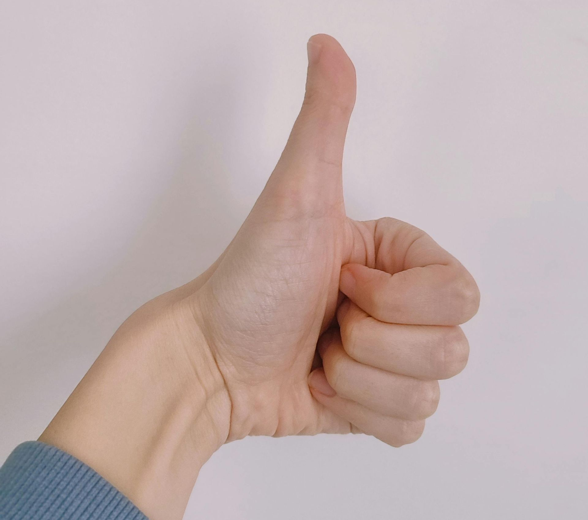 Een close-up van een menselijke hand die een duim omhoog steekt tegen een effen witte achtergrond.