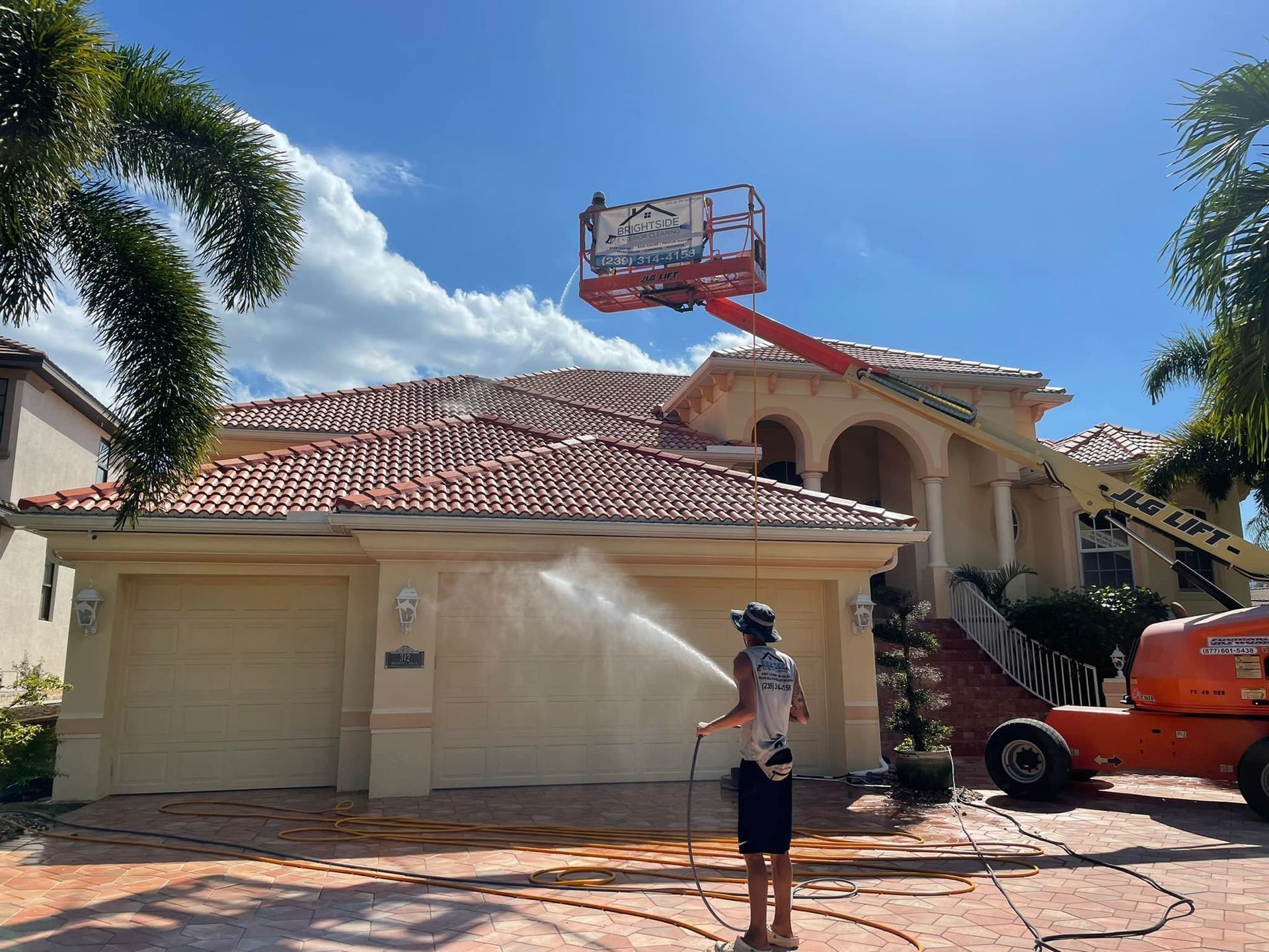 A man is cleaning the roof of a house with a hose.