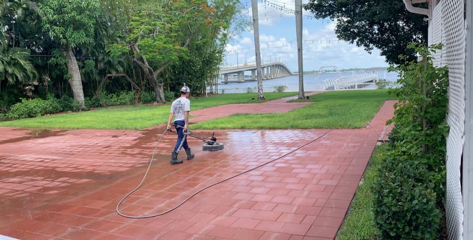 A man is cleaning a brick driveway with a pressure washer.