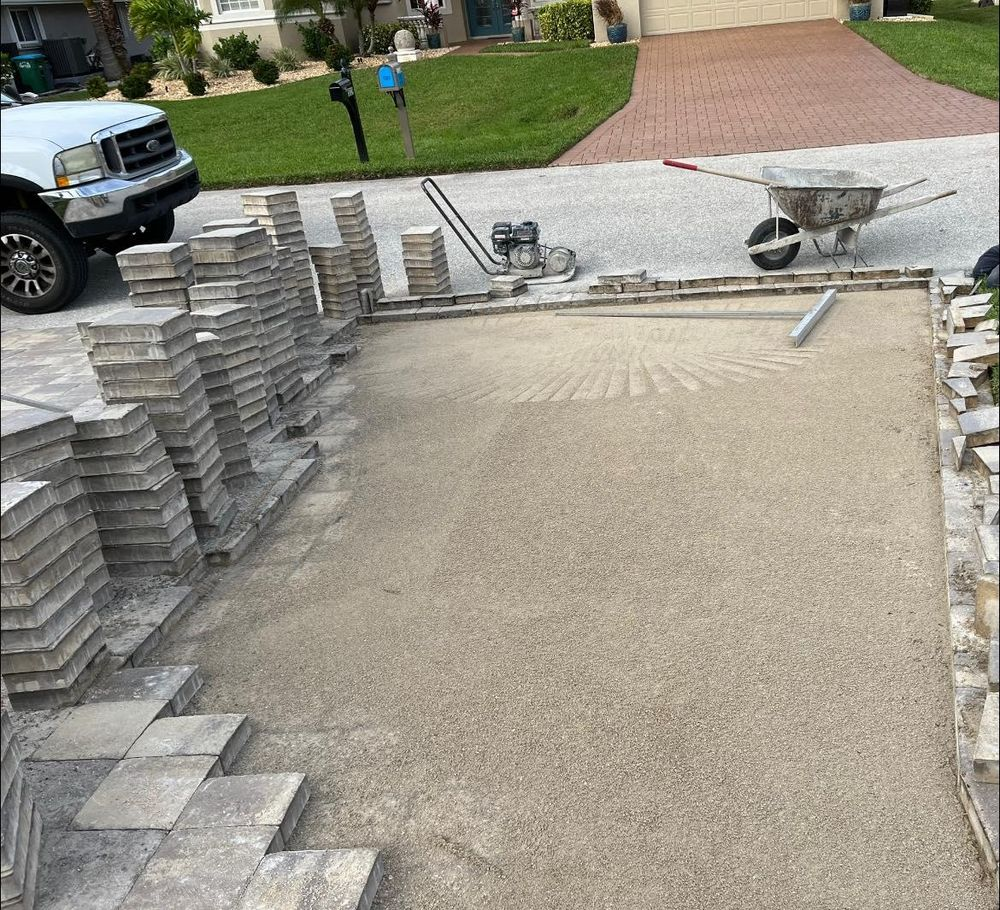 A truck is parked in a driveway next to a wheelbarrow filled with bricks.