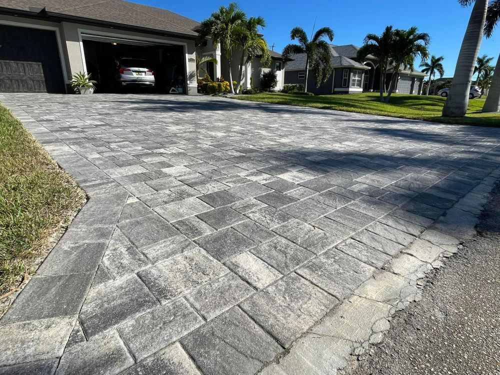 A brick driveway leading to a house with a car parked in the garage.
