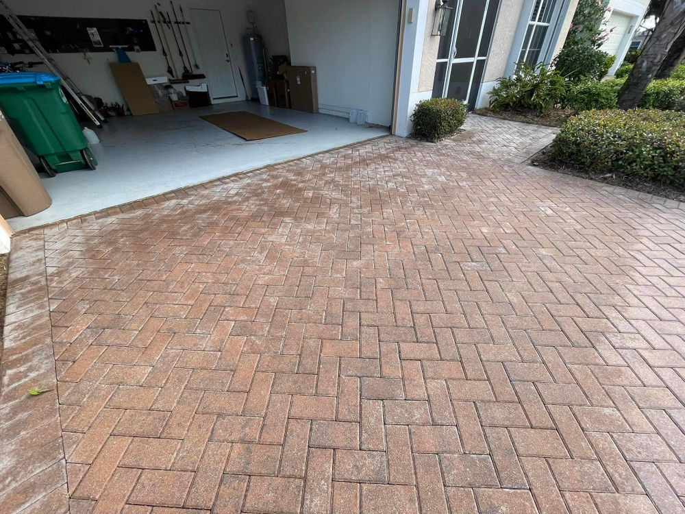 A brick driveway leading to a garage with a green trash can.