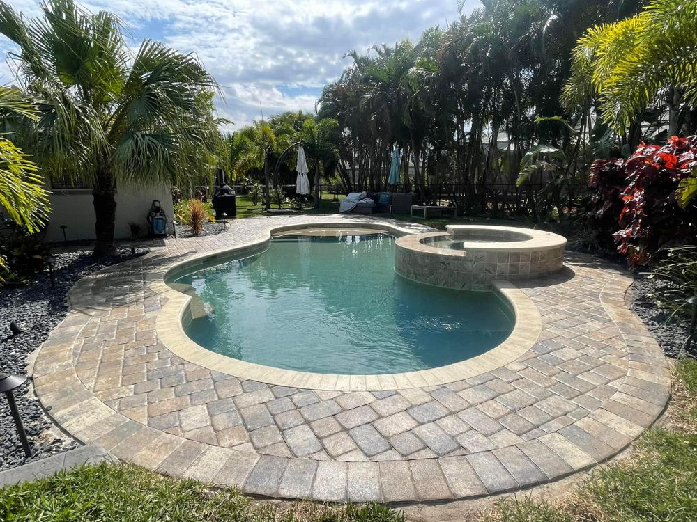 A large swimming pool surrounded by palm trees and a brick patio.