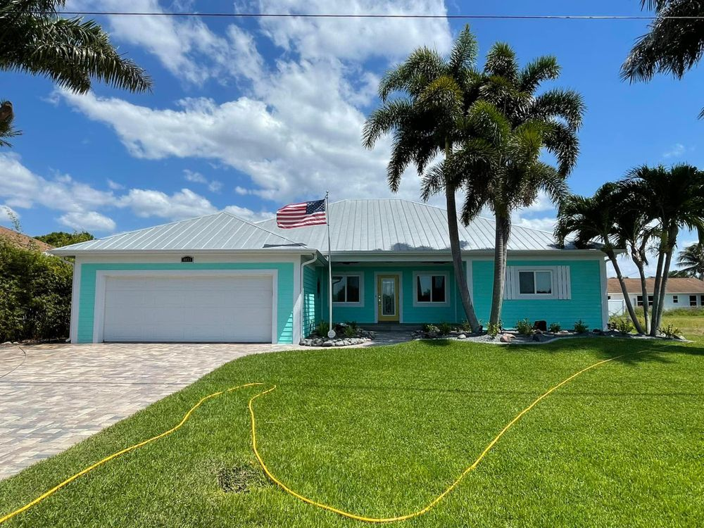A blue house with a white garage door and palm trees in front of it.