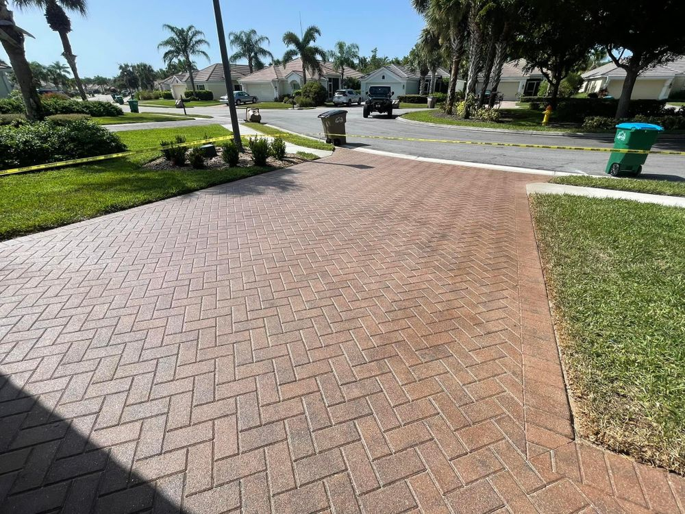 A brick driveway with a green trash can in the middle of it.