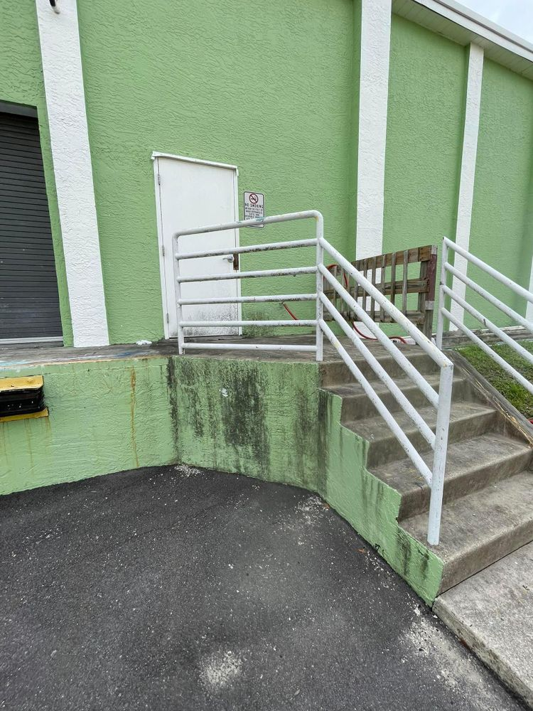 A green building with stairs leading up to it and a white railing.