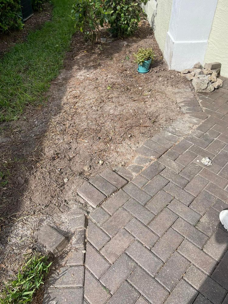 A person is standing on a brick patio next to a grassy area.