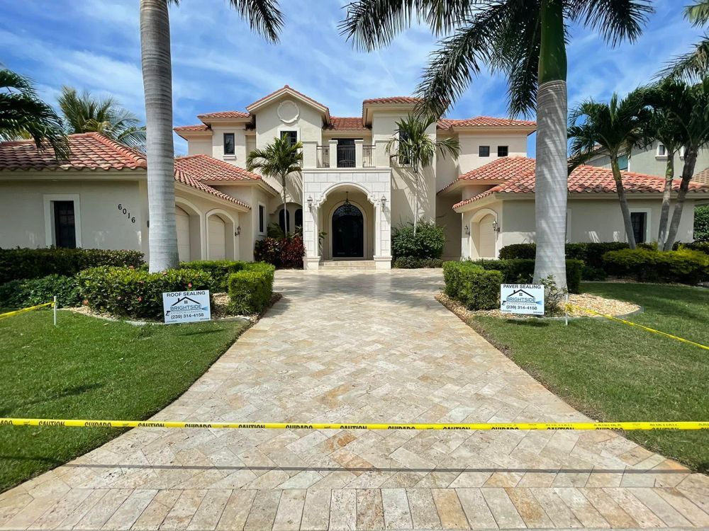 A large white house with a brick driveway and palm trees in front of it.