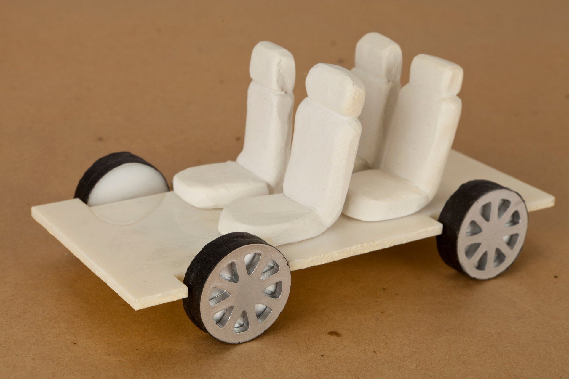 Wooden model car with four white seats and silver-rimmed wheels.