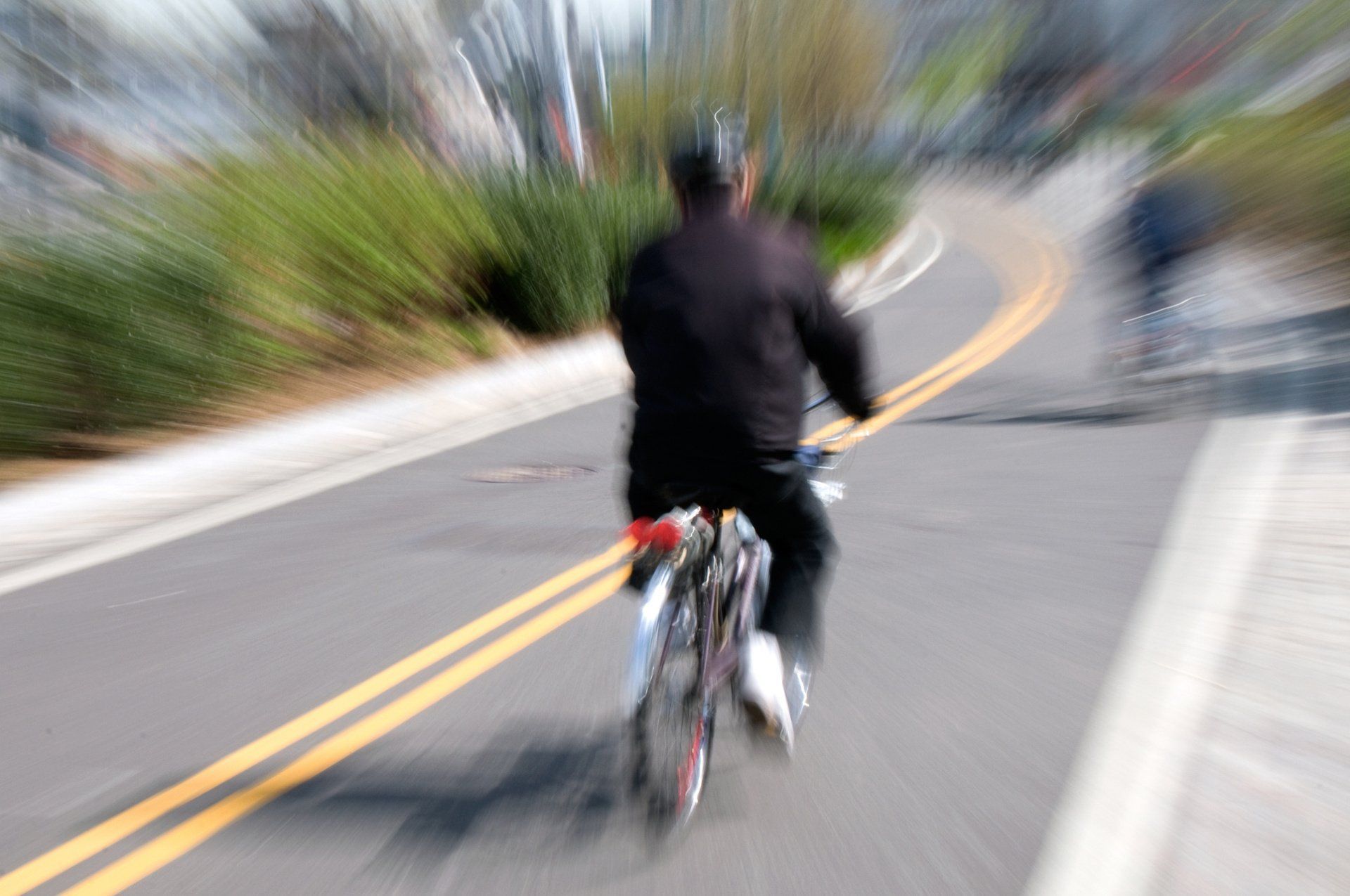Cyclist riding fast on a road with yellow lines, blurred motion, sunny day.