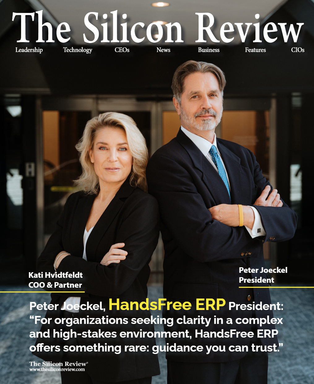 Two business leaders in suits pose on The Silicon Review cover, arms crossed, in a dark office setting