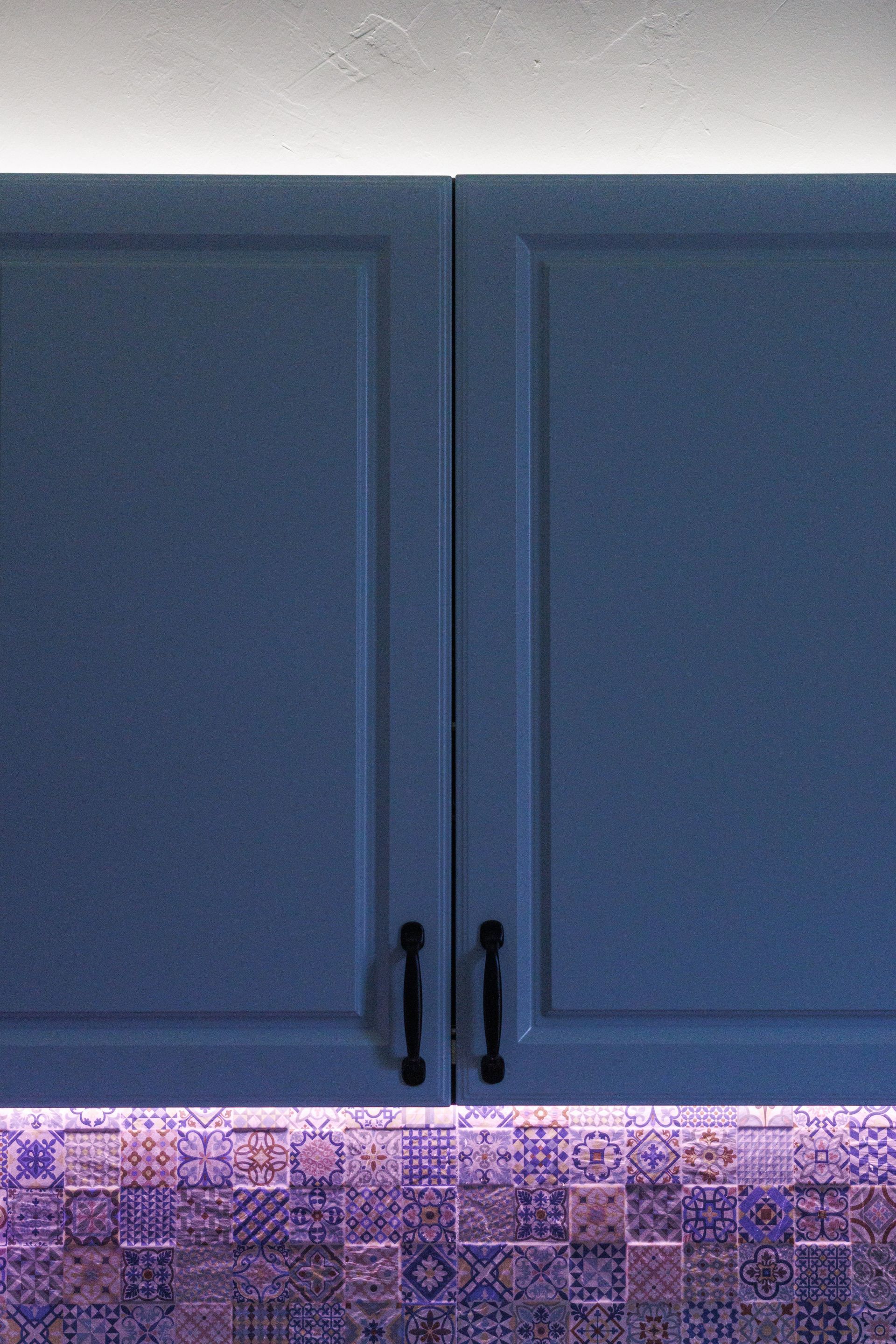 Blue kitchen cabinets with black handles above a lit patterned backsplash