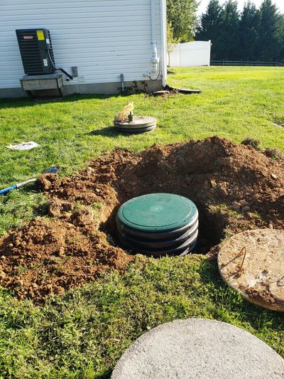 Three black plastic septic tanks installed in a dirt excavation with green lids and orange pipes.