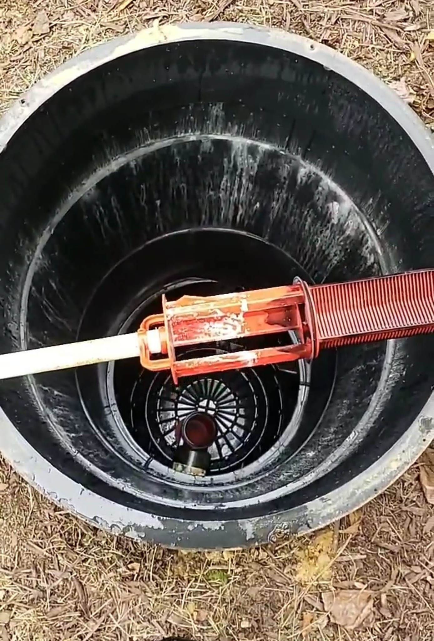 Inside view of a black well, a red pump is positioned over the water.