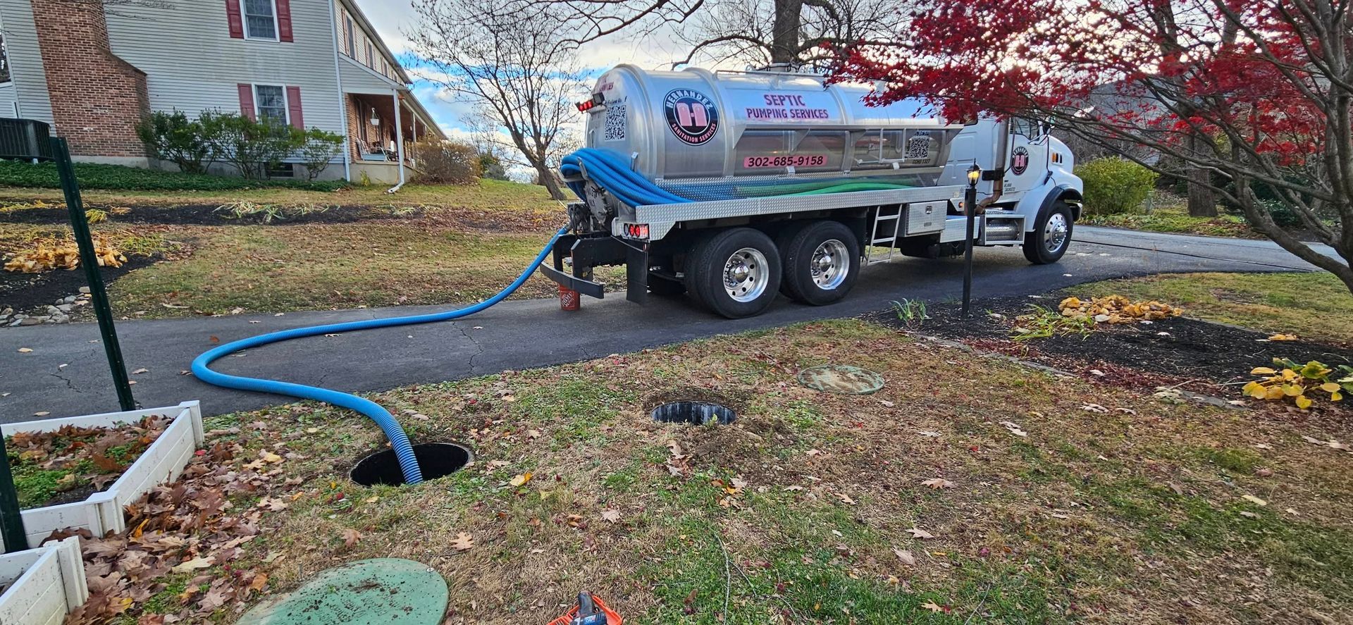 Septic tank pumping truck with hose extending into a manhole in a residential yard.