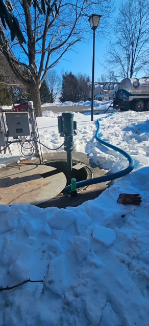 Person pumping out a septic tank in a yard with green grass and foliage.