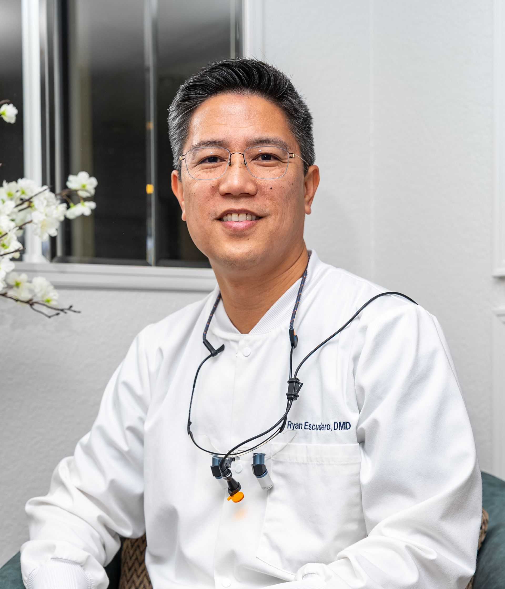 Man wearing glasses and a white lab coat smiles in a dental office.