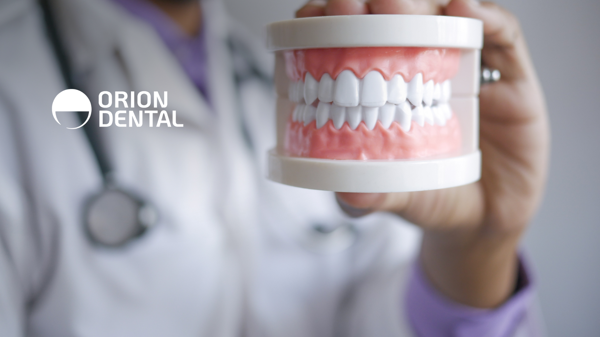 A dentist holding a model of teeth, with the Orion Dental logo in the corner.