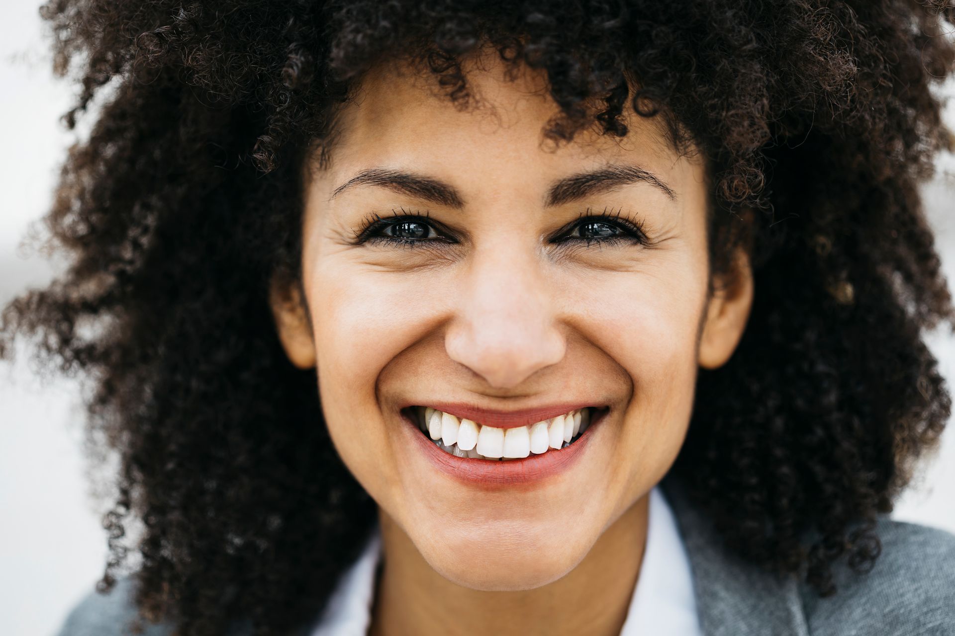 Woman with curly hair smiles broadly, showing teeth.