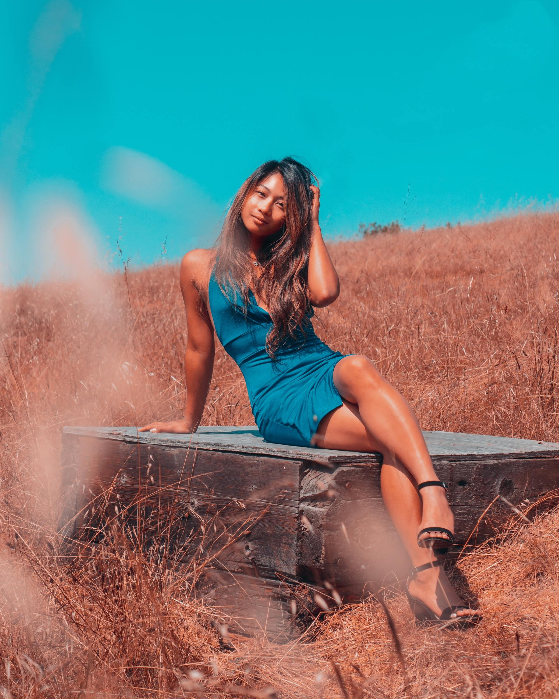A woman in a blue dress is sitting on a bench in a field.