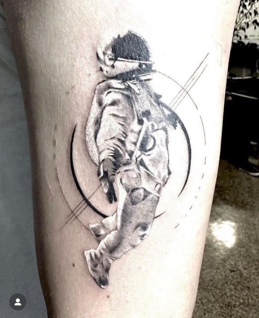 Tattoo of an astronaut floating, detailed black and white with geometric lines and circles on arm.