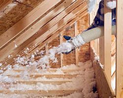 Worker in hard hat spraying insulation into wall studs of a house under construction