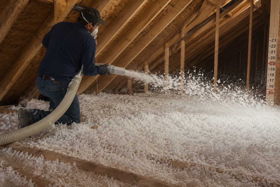 Worker spraying insulation into attic rafters with a foam hose