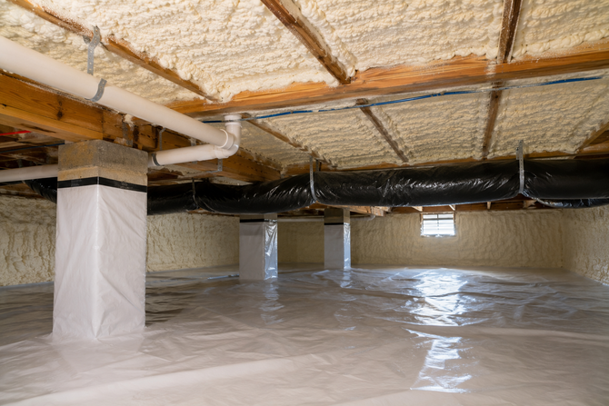 Worker in orange hard hat spraying foam insulation inside a building frame