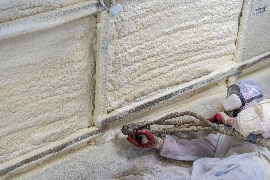 Worker spray-applying foam insulation inside a wall cavity with a handheld nozzle.