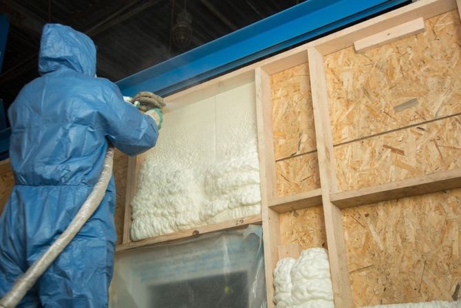 Worker in hard hat and respirator inspecting insulation inside a building frame