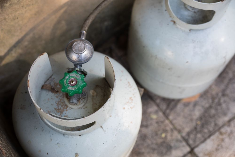 Two white propane tanks with green valves on a tiled floor. — D & E Milner Plumbing In The Palms, QLD