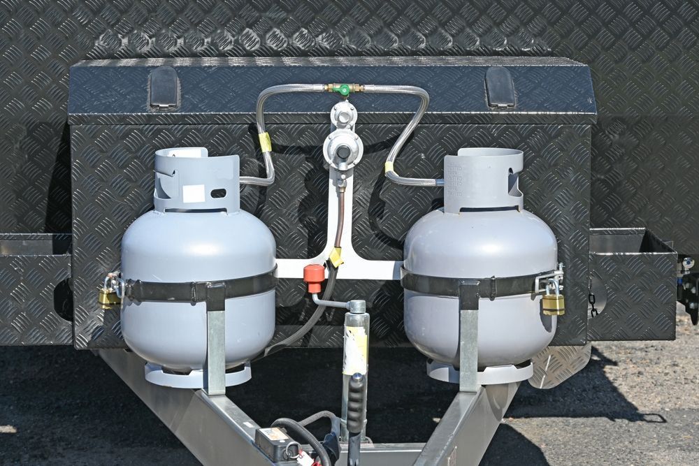 Two grey propane tanks secured on a trailer with a regulator and connecting lines.