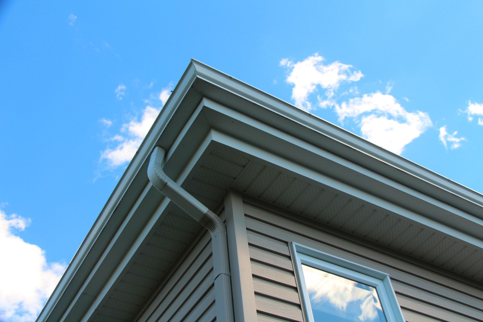 Corner of a house with light brown siding, white trim, and a gutter against a blue sky with clouds — D & E Milner Plumbing In The Palms, QLD