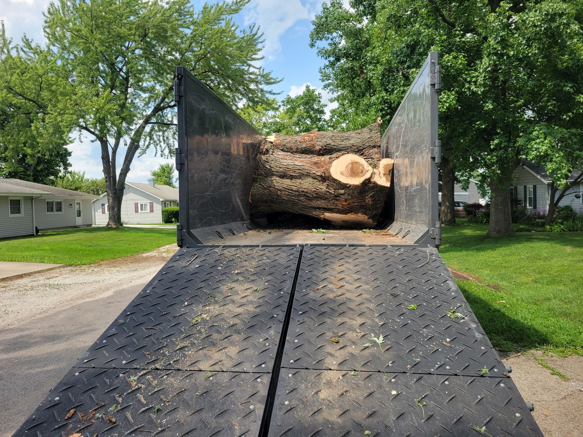 A large log inside a truck bed, ready for transport, parked on a residential street.