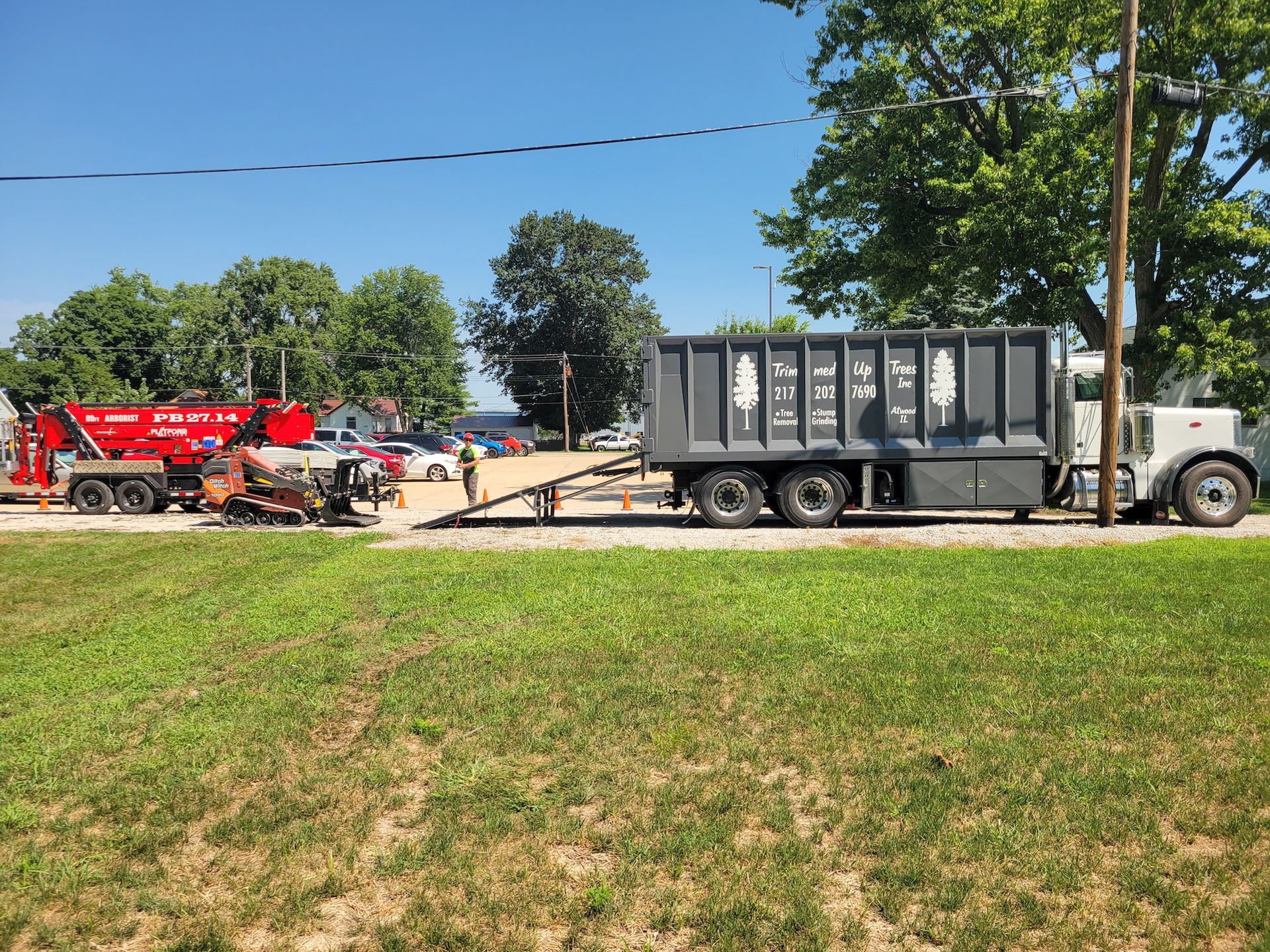 Two large trucks, a red one towing equipment, and a grey one with a container, parked outdoors on a sunny day.