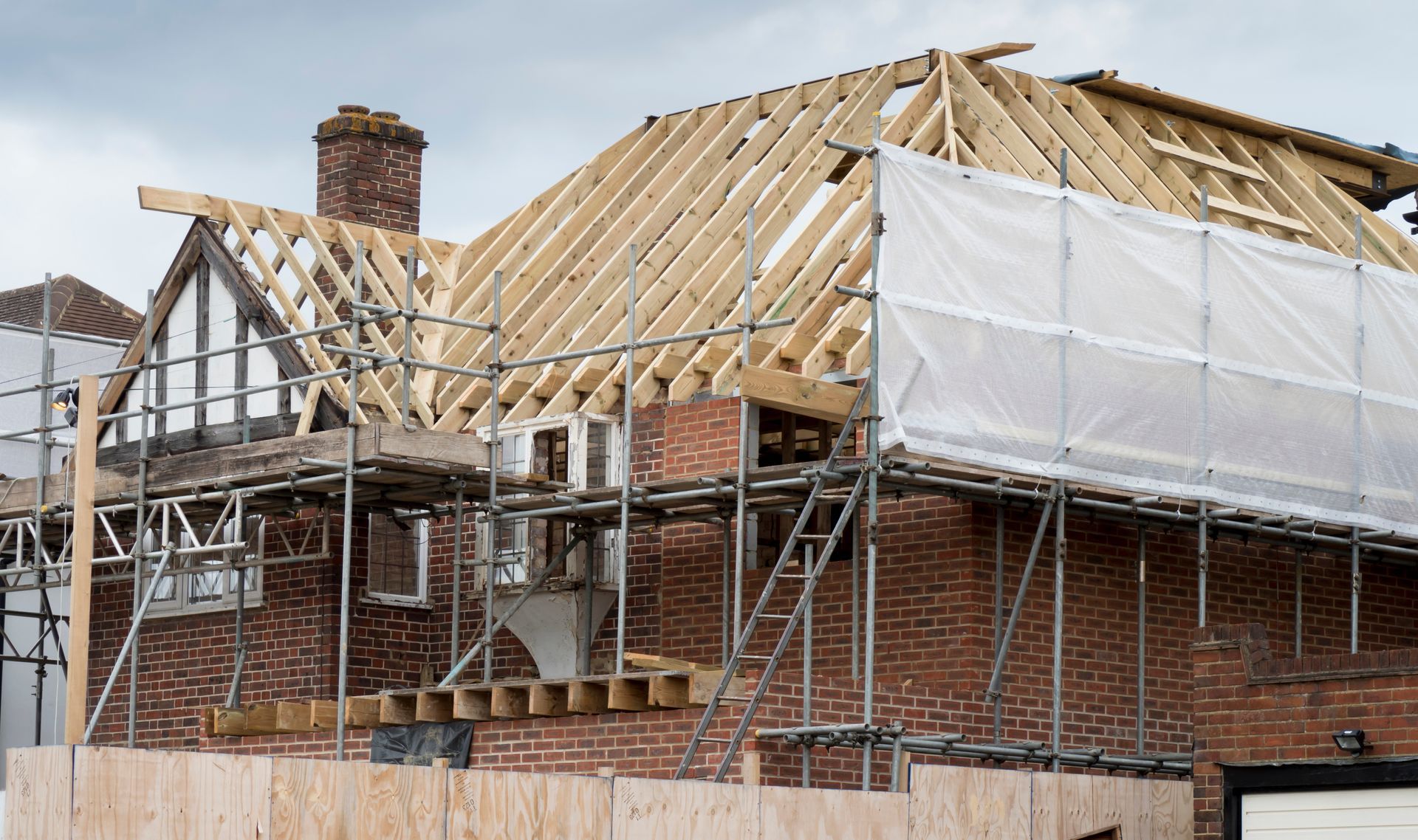 Maison en briques en cours de construction de toiture avec échafaudage et charpente en bois.