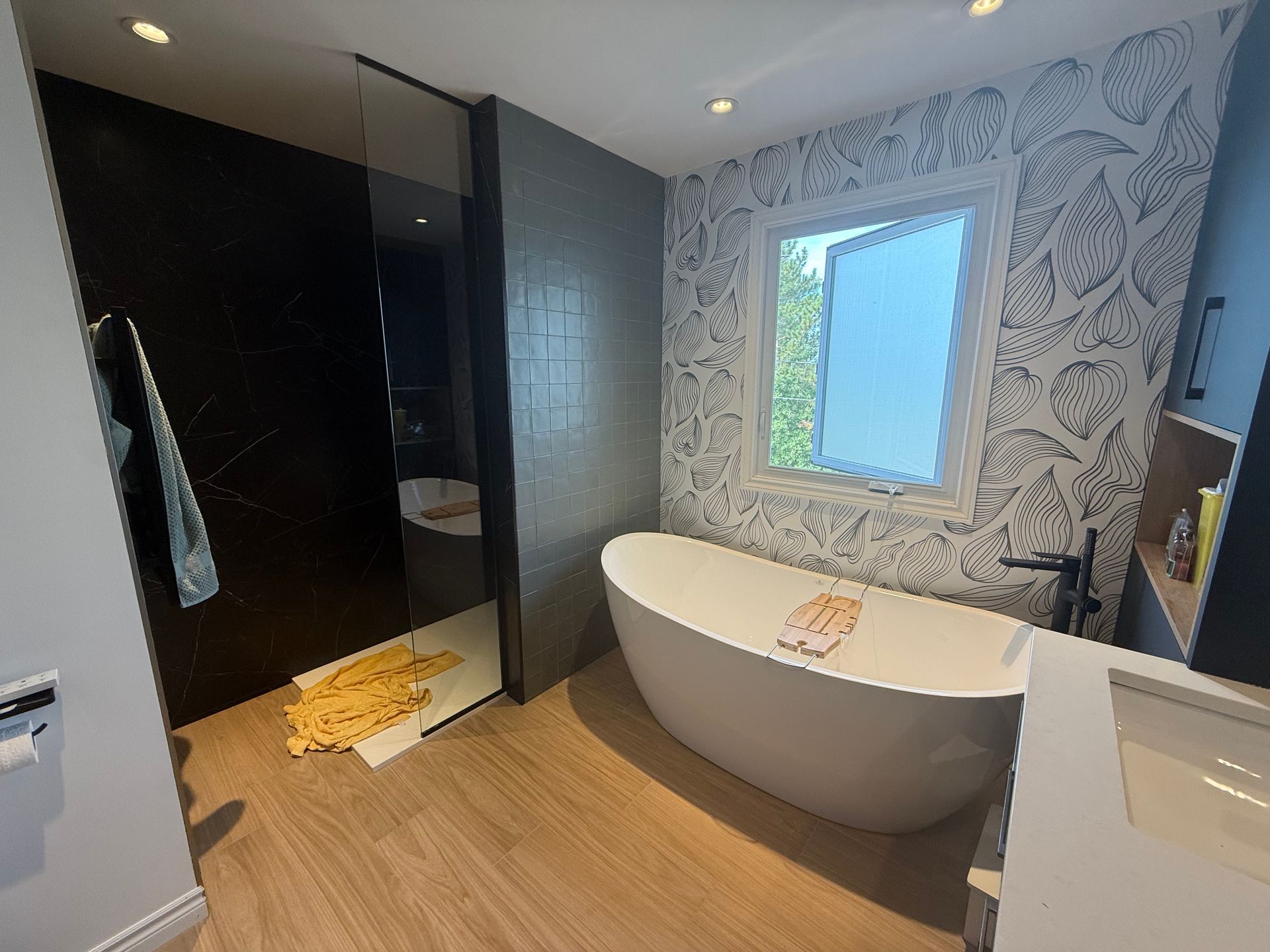 Salle de bain moderne avec baignoire blanche, mur à motifs et douche en verre.