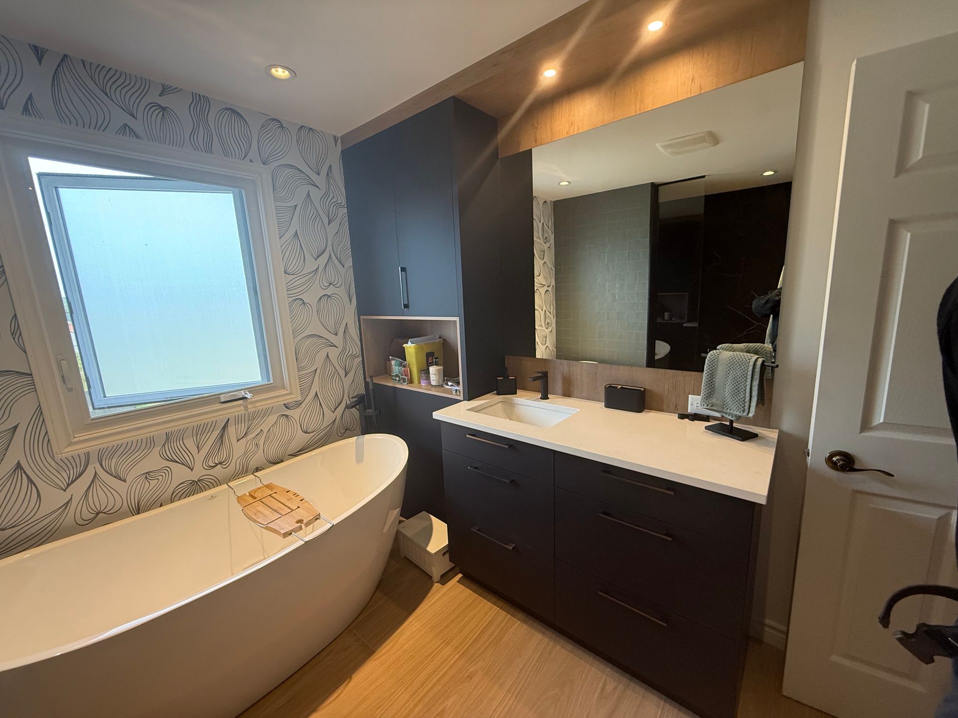 Salle de bain avec baignoire blanche, vanité foncée et papier peint floral.