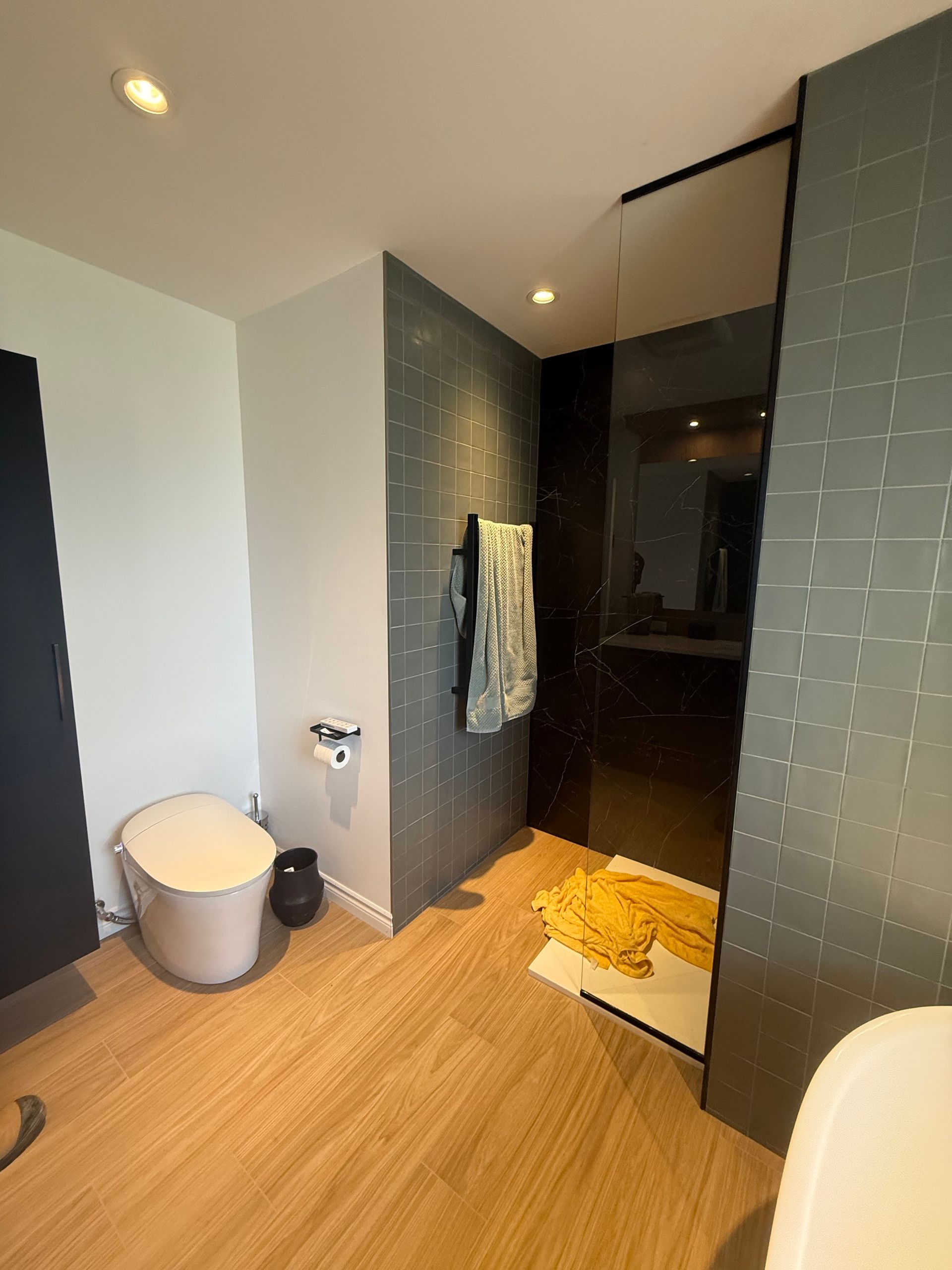 Salle de bain moderne avec toilettes, douche et sèche-serviettes. Carrelage gris foncé et parquet clair.
