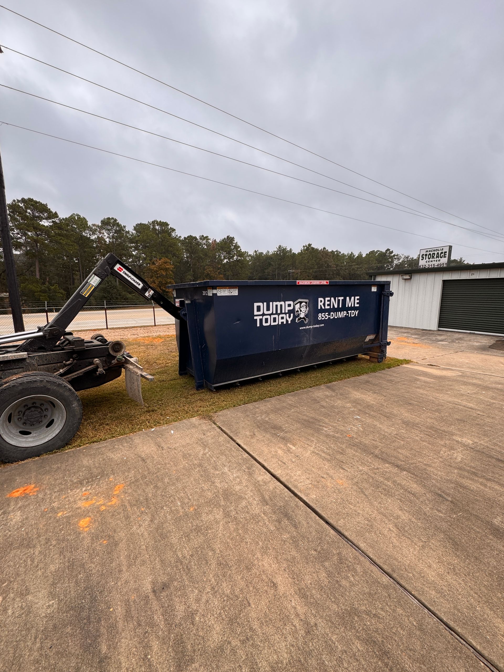 Dump Today LLC 20-yard navy blue roll-off dumpster with RENT ME branding, being delivered by a hook-lift truck in a storage facility parking lot in Houston TX