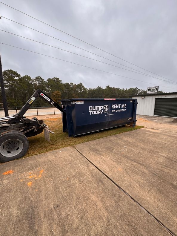 Dump Today LLC 20-yard navy blue roll-off dumpster with RENT ME branding, being delivered by a hook-lift truck in a storage facility parking lot in Houston TX