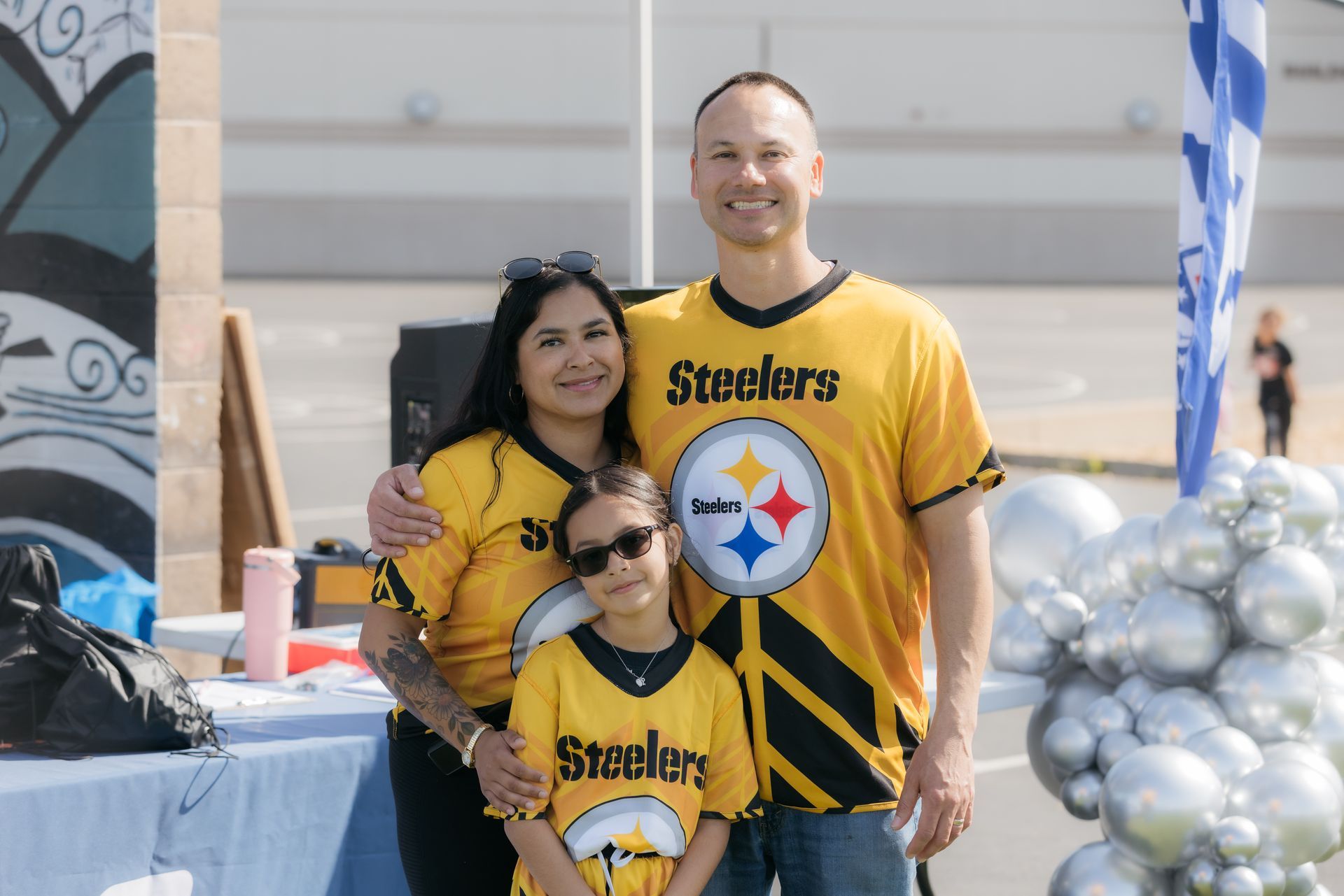Three people in Steelers jerseys posing at an outdoor event with silver balloons