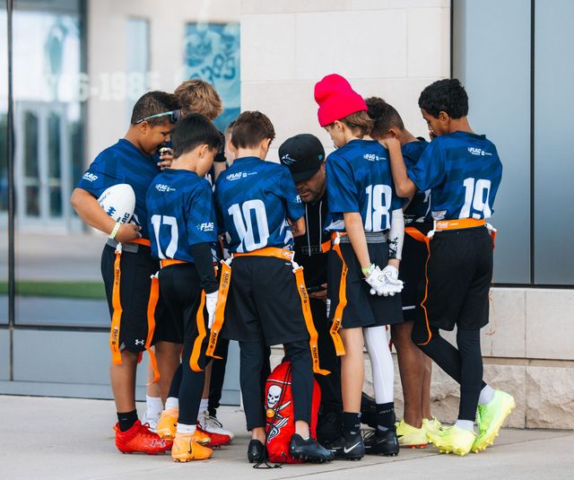 Youth soccer team huddled together in blue jerseys before a game, one wearing a red beanie