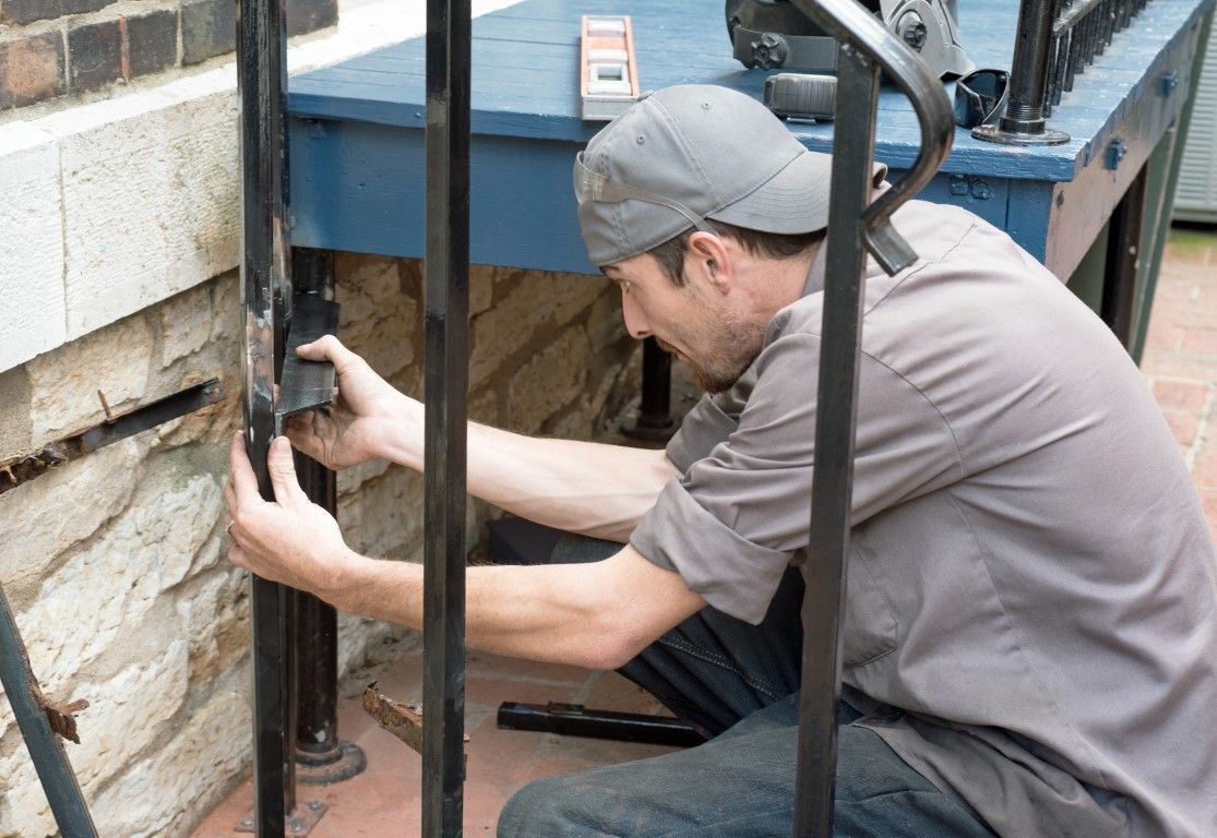 Worker kneels by a brick wall, adjusting a black metal railing or fence post.