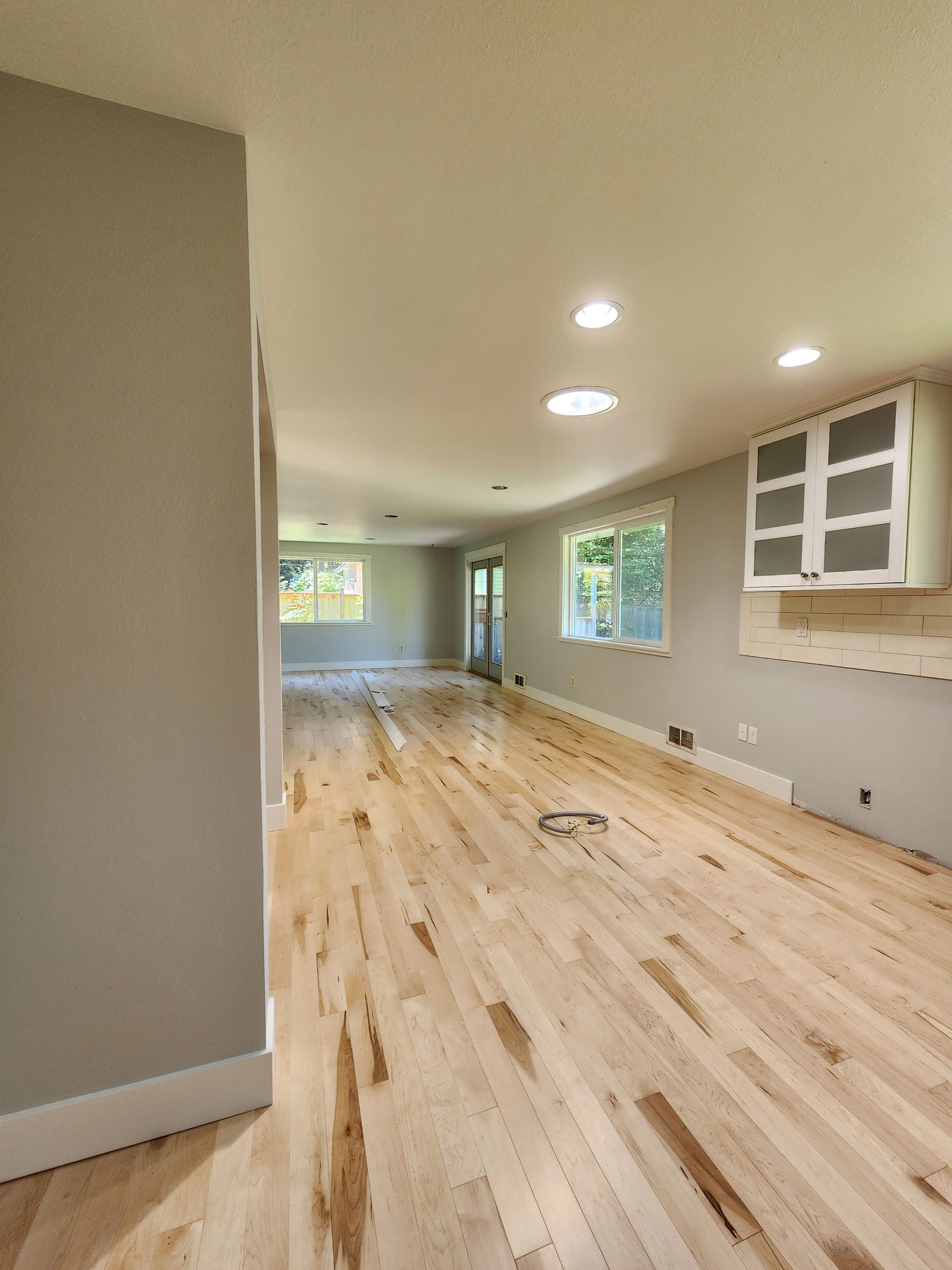 Empty room with light wood floors, gray walls, and recessed lighting. A small cabinet sits on the wall.